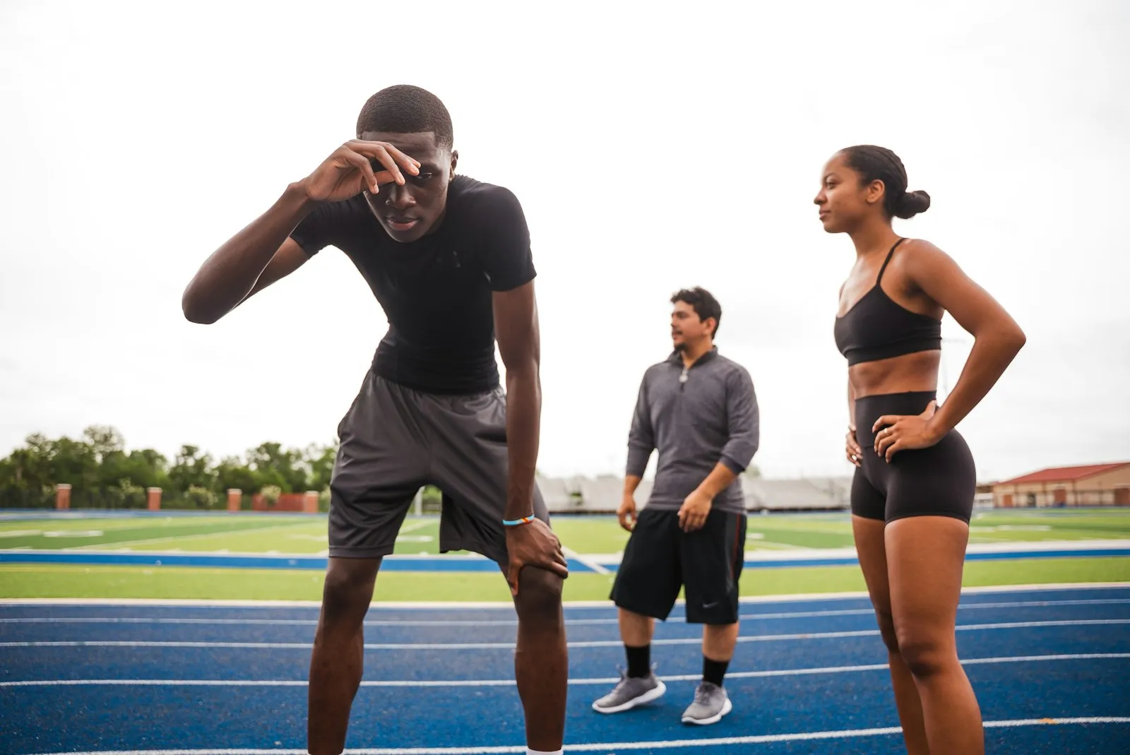 Three athletes on a blue running track, one catching his breath